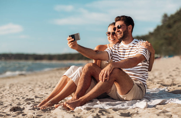 happy couple taking selfie by smartphone on beach - 写真・画像