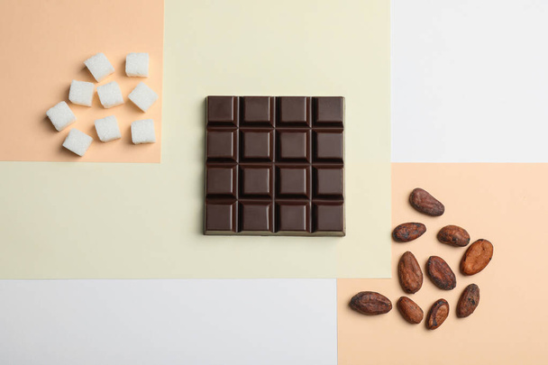 Delicious dark chocolate bar, refined sugar and cocoa beans on color background, flat lay - Foto, Imagem