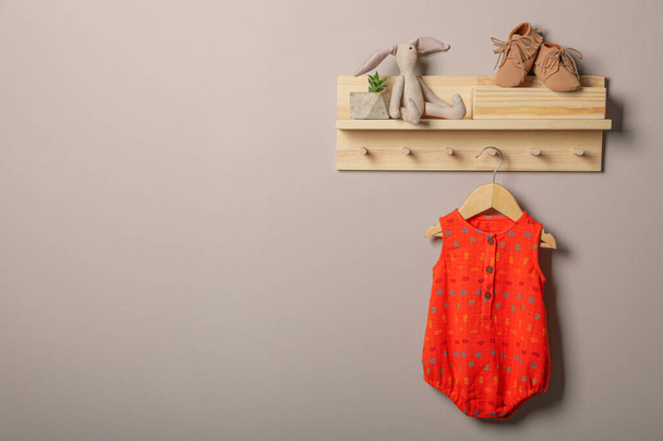 Baby bodysuit, booties and toy on wooden rack. Space for text - 写真・画像