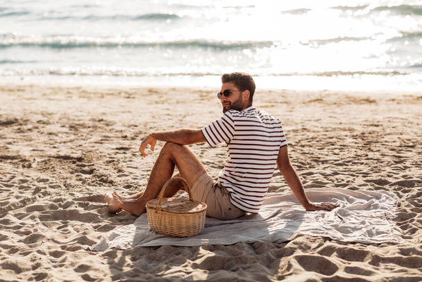 man with picnic basket on blanket on summer beach - Fotó, kép
