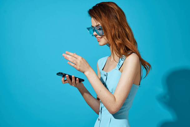 portrait of a woman in a blue dress with phone in hand blue background - Фото, изображение