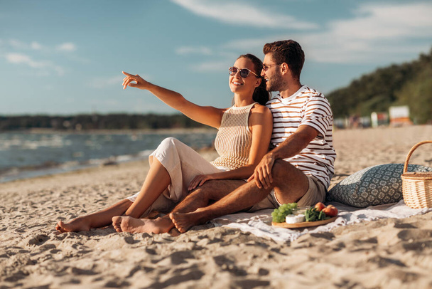 happy couple with food having picnic on beach - Zdjęcie, obraz