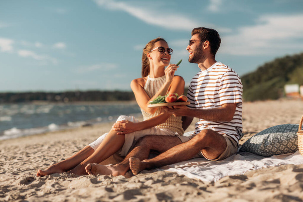 happy couple with food having picnic on beach - Фото, изображение