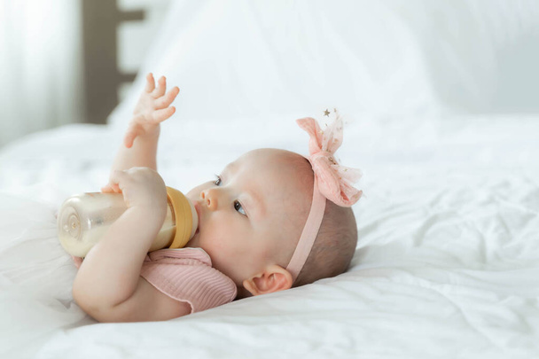The newborn Adorable baby drinking milk from bottle on a white bedroom  - Foto, Bild