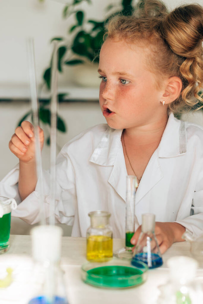 Little red-haired girl in white uniform conducting chemical experiments in a laboratory.Back to school concept.Young scientists.Natural sciences.Preschool and school education of children. - Φωτογραφία, εικόνα