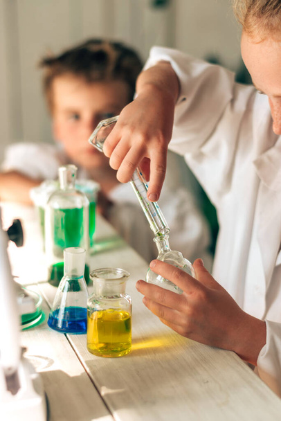 Serious little boy and girl in white uniforms conducting chemical experiments in a laboratory.Back to school concept.Young scientists.Natural sciences.Preschool and school education of children. - Valokuva, kuva