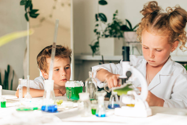 Little boy and girl in white uniforms look into the microscope in a laboratory.Back to school concept.Young scientists.Natural sciences.Preschool and school education of children. - Photo, Image