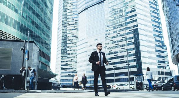 Busy young male office worker in trendy formal style clothing going to work with modern buildings on background at downtown - Фото, изображение