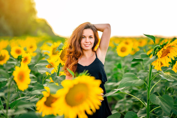 A charming young woman in a dress in a field of sunflowers. A beautiful concept of a summer holiday - Foto, Bild