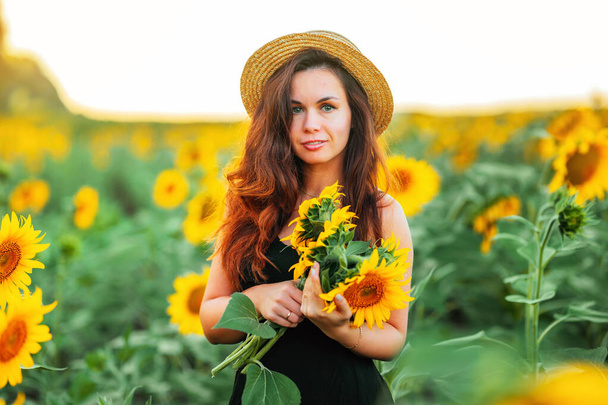 A charming young woman in a dress in a field of sunflowers. A beautiful concept of a summer holiday - Φωτογραφία, εικόνα