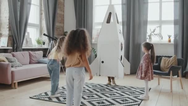 Портативный снимок группы милых маленьких детей, играющих с моделью картонного ракетного корабля дома - Кадры, видео