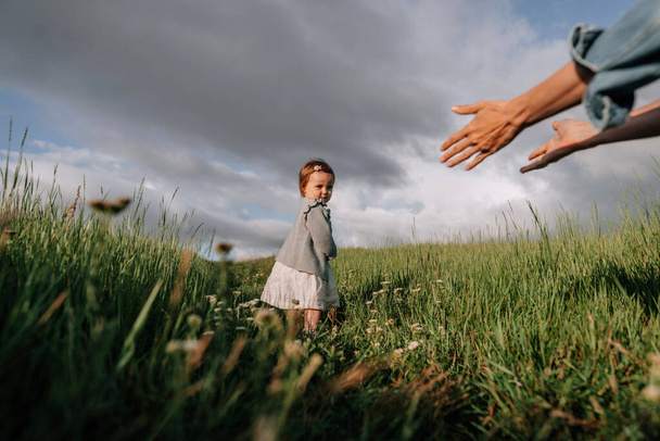 Toddler elsétál az anyjától a szabadban. Fiatal nő kinyújtja a kezét a kislánynak.. - Fotó, kép
