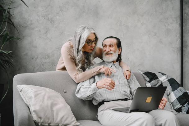 Starsza para siedzi na kanapie z laptopem - Zdjęcie, obraz