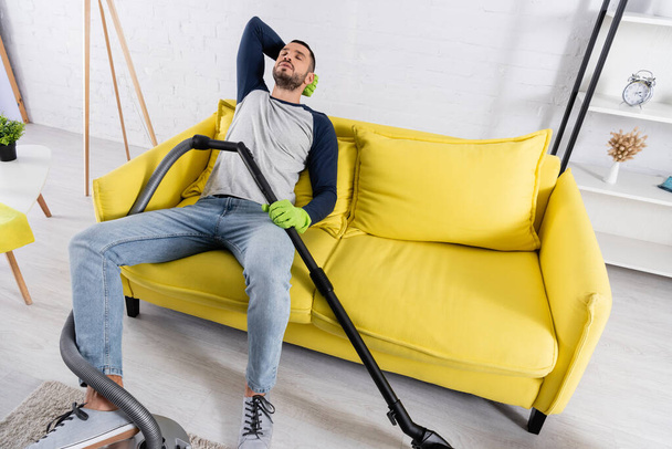 High angle view of tired man in rubber gloves holding vacuum cleaner  - Fotografie, Obrázek