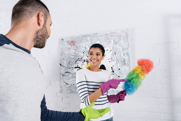 Cheerful african american woman pointing at dust brush near boyfriend  - Photo, Image