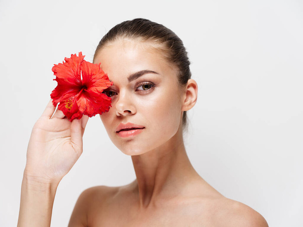 portrait of pretty woman with red flower near face on light background  - Foto, imagen