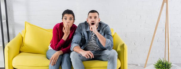 Astonished couple with remote controller sitting on couch, banner  - Photo, image
