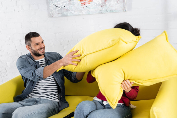 Travesseiro homem positivo lutando com a namorada afro-americana na sala de estar  - Foto, Imagem