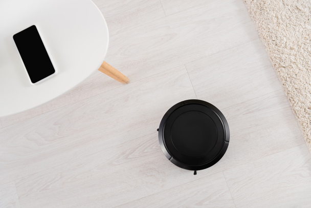 Top view of robotic vacuum cleaner and smartphone at home  - Photo, Image