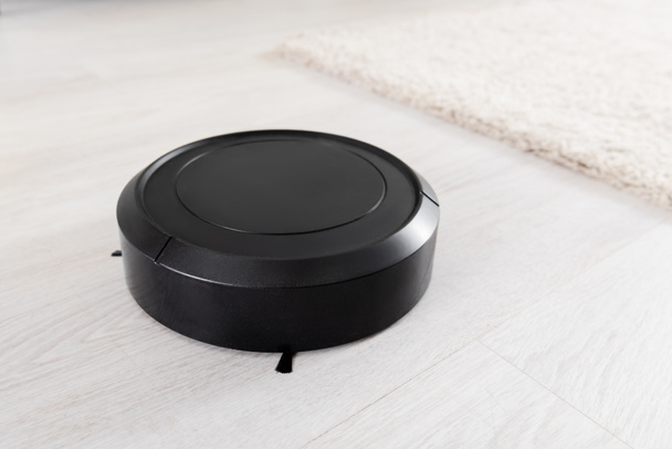Close up view of robotic vacuum cleaner near blurred carpet on floor  - Photo, Image