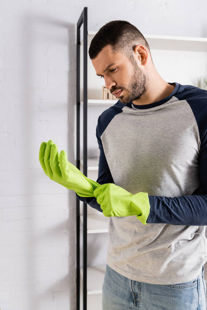 Young man wearing rubber gloves at home  - Фото, изображение
