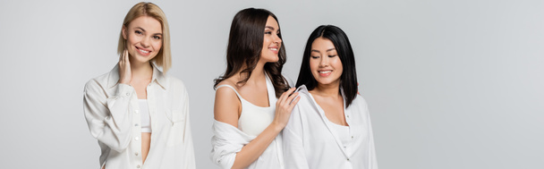 joyful interracial young models in white shirts posing isolated on grey, banner - Zdjęcie, obraz