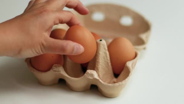 Hnědá organická kuřecí vejce v hnědém papírovém tácu na bílém stole. Zdravé potraviny a organické proteinové snídaně koncept - Záběry, video