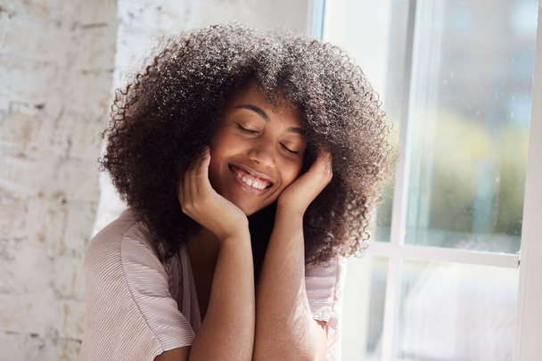 Pihentető mosolygós fiatal afro-amerikai nő ül az ablak mellett - Fotó, kép