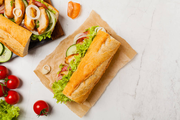 Chicken sandwich with tomato, cucumber, lettuce and onions. White stone background. Top view. Flat lay. - Photo, image