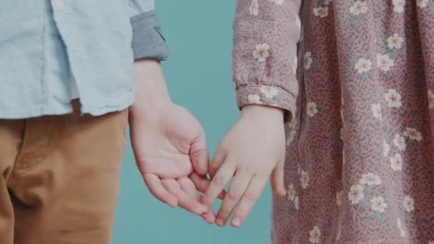 Κοντινό πλάνο στη μέση της τομής του αγνώριστο μικρό αγόρι και κορίτσι κρατώντας τα χέρια πάνω σε μπλε φόντο - Πλάνα, βίντεο