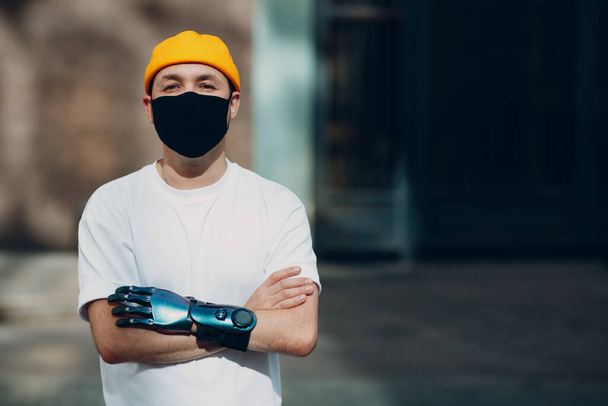 Young disabled man with artificial prosthetic hand wearing medical protective face mask. - Photo, Image
