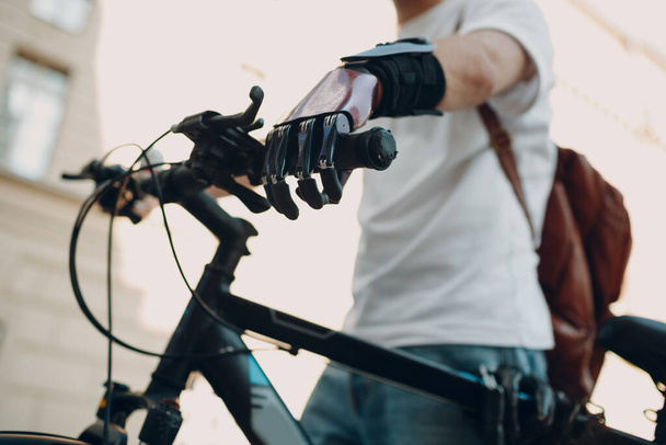 Joven hombre discapacitado con la mano prótesis artificial en ropa casual montar en bicicleta. - Foto, Imagen