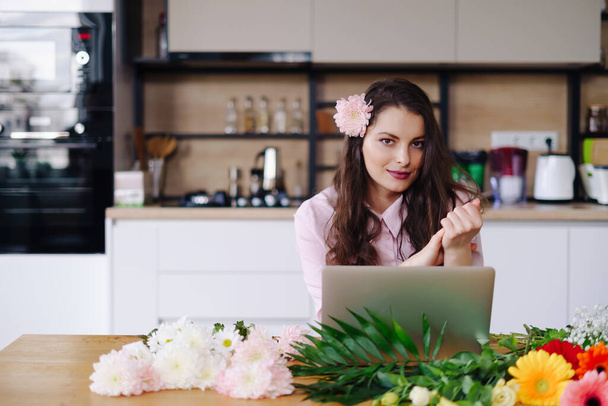 Portrait of working burly brunette with flowers and laptop at table - Photo, Image