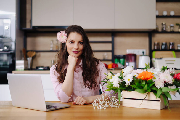 Portrait of working burly brunette with flowers and laptop at table - Foto, afbeelding