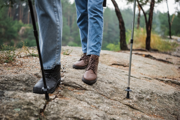 vista cortada de jovem casal de pé com caminhadas varas em solo rochoso  - Foto, Imagem