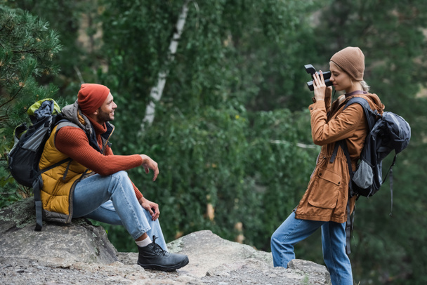 Frau mit Rucksack fotografiert glücklichen Freund vor Oldtimer-Kamera im Wald  - Foto, Bild