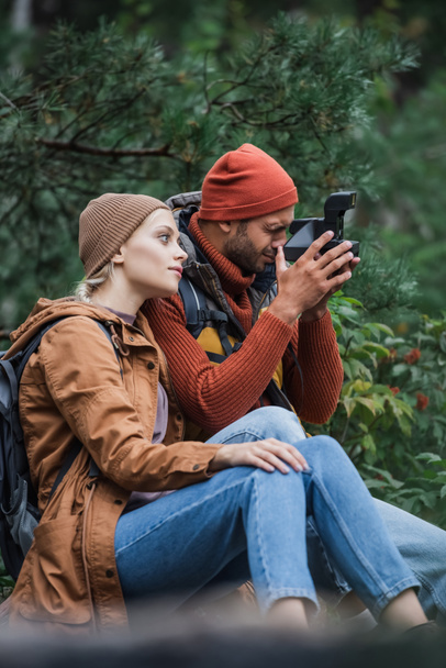 woman sitting with boyfriend taking photo on vintage camera in forest  - Photo, Image