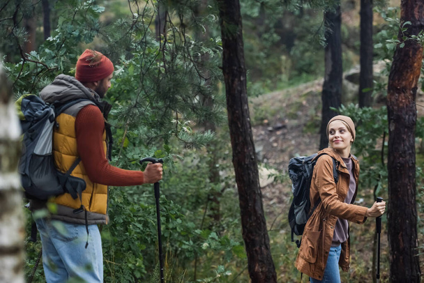 pleased couple looking at each other trekking with hiking sticks in forest  - Foto, Imagen