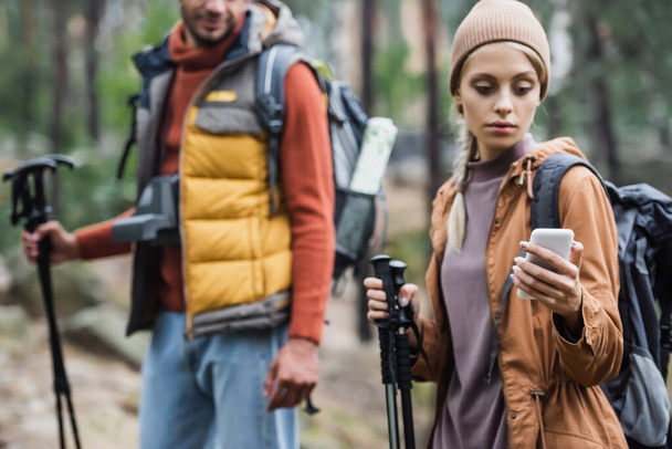žena držící smartphone při hledání v blízkosti rozmazané přítel - Fotografie, Obrázek