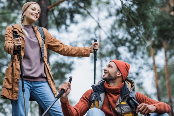 happy couple with hiking sticks resting after trekking in forest  - Foto, Imagem