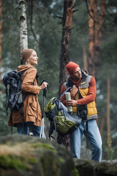 man holding map and backpack near cheerful woman with hiking sticks - Photo, Image