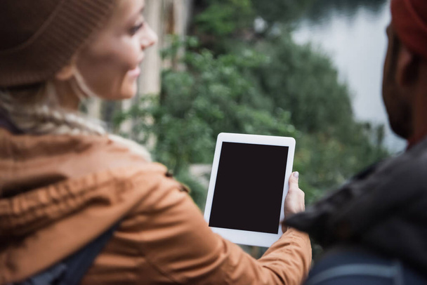 mujer borrosa y feliz sosteniendo tableta digital con pantalla en blanco cerca de novio en el bosque  - Foto, Imagen
