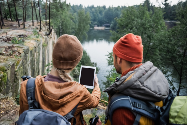 back view of woman holding digital tablet with blank screen near boyfriend in forest near lake - Foto, afbeelding