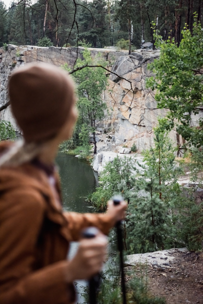 Вид сзади размытой женщины, стоящей с тростями у скалы и озера - Фото, изображение