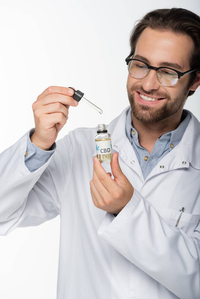 smiling doctor holding vial and dropper of cbd oil isolated on white - 写真・画像