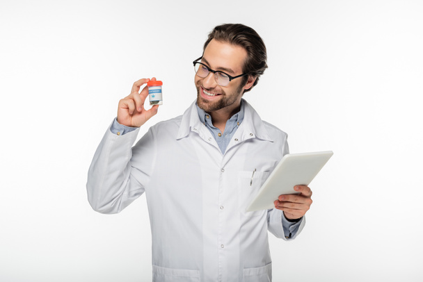 uśmiechnięty lekarz trzymający cyfrowe tabletki i pojemnik z suchą medyczną marihuaną wyizolowaną na białym - Zdjęcie, obraz