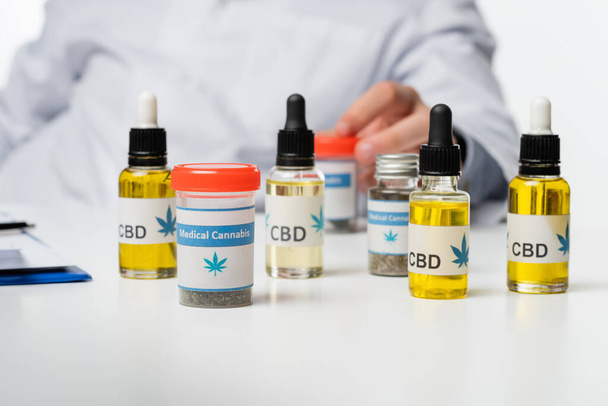 vista recortada de un médico borroso cerca de contenedores y viales con medicamentos de cannabis medicinal aislados en blanco - Foto, imagen