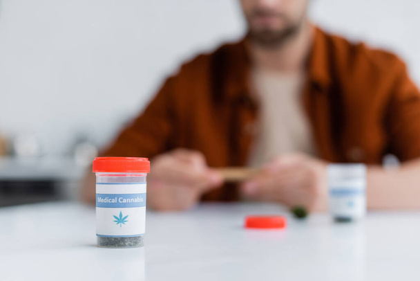 selective focus of container with dry medical cannabis near blurred man - Valokuva, kuva