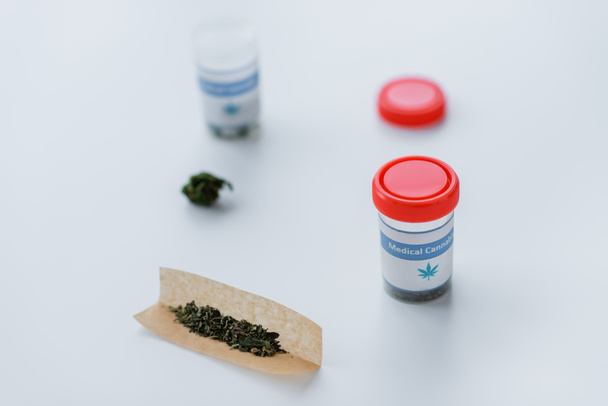recipientes y papel de cigarrillo con cannabis medicinal seco en escritorio blanco - Foto, Imagen