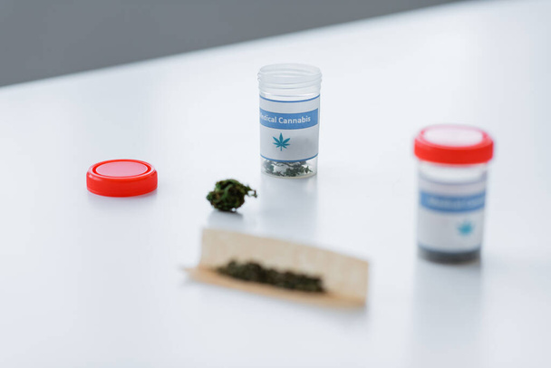 containers and cigarette paper with dry medical cannabis on white desk - 写真・画像